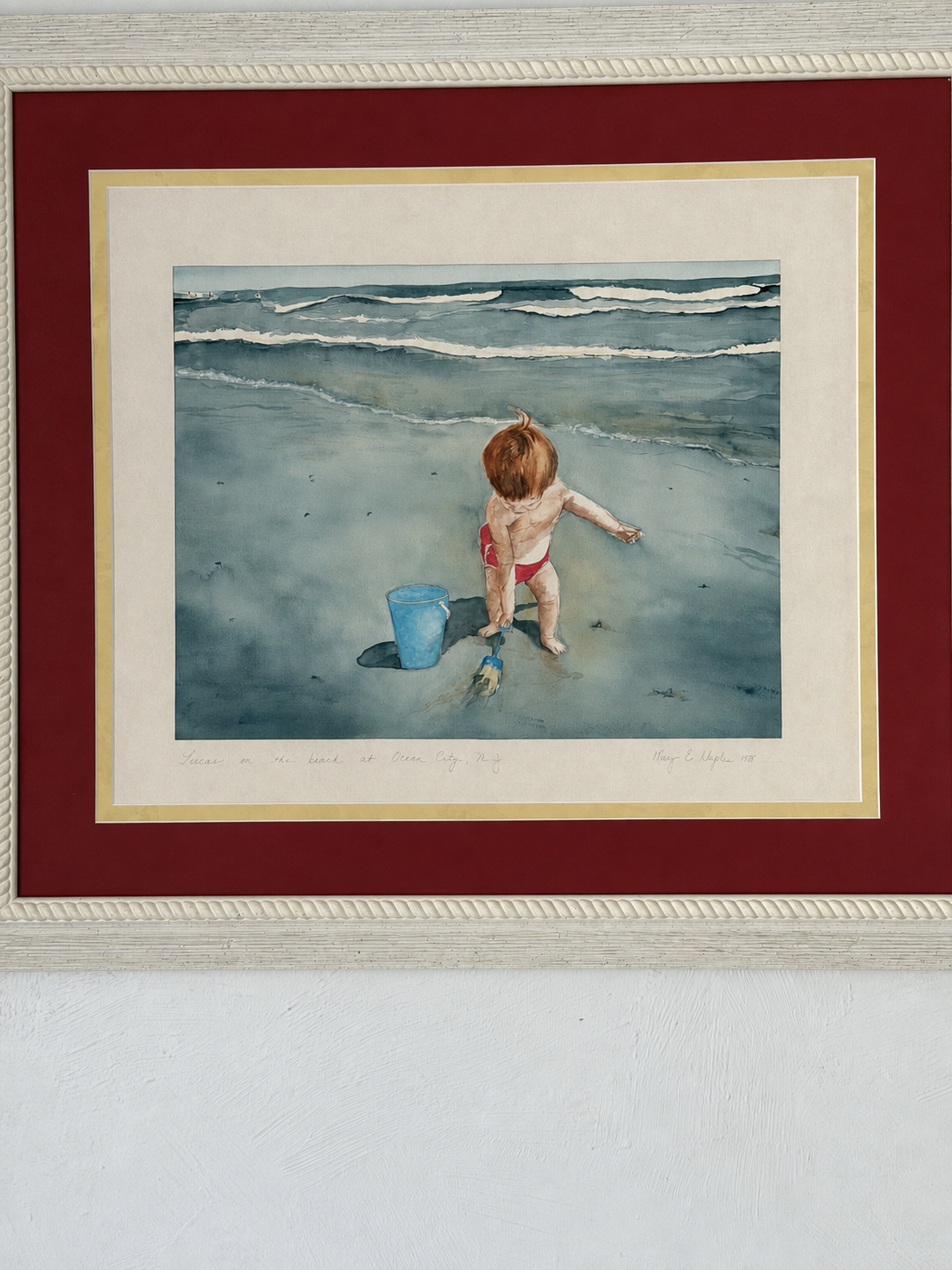 Framed coastal painting of a small child with a bucket at the water's edge