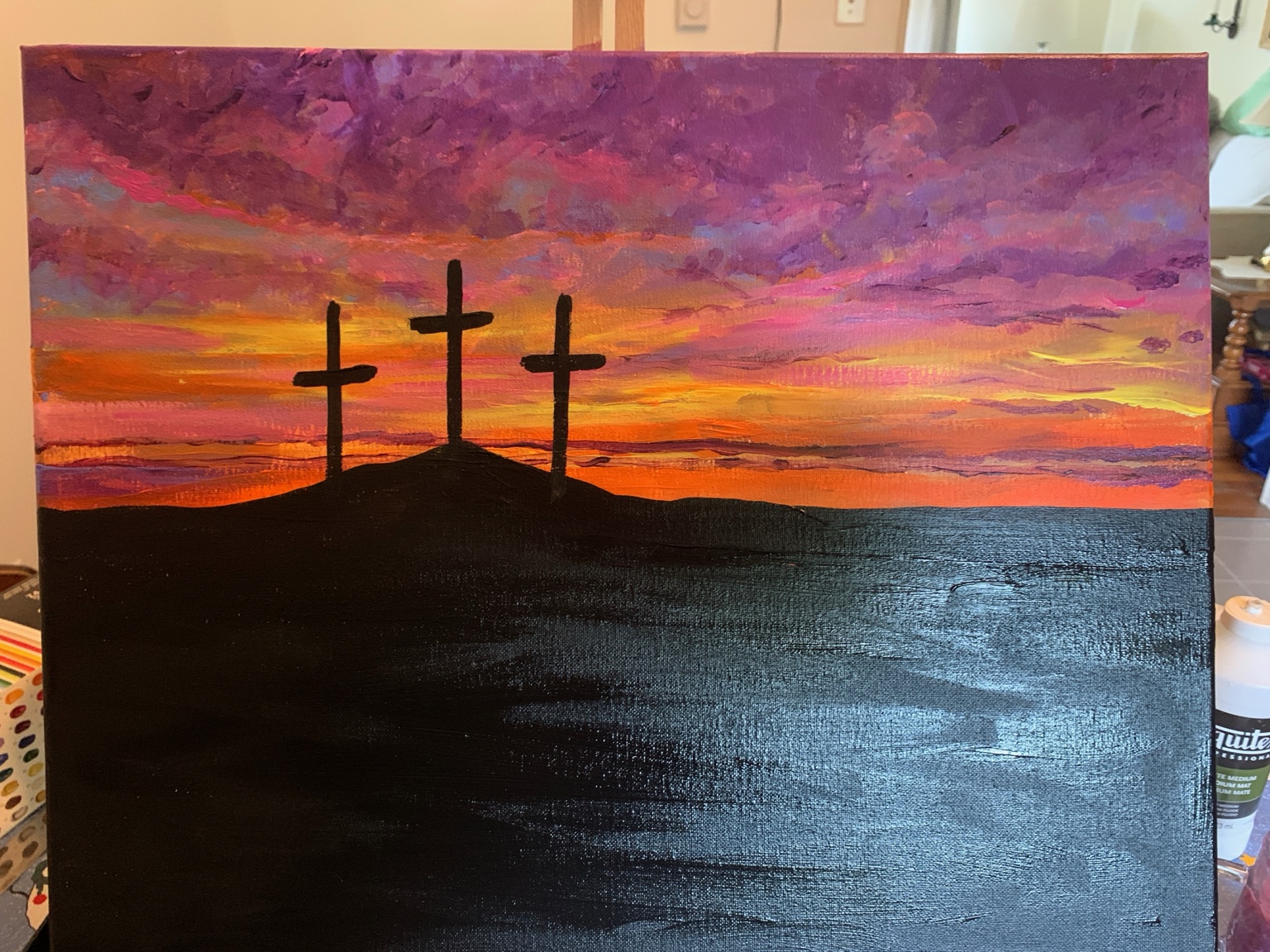 Three crosses silhouetted on a hill beneath a vivid purple, pink, and orange sunset